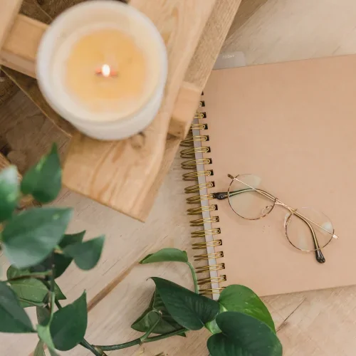 Candela accesa, quaderno e occhiali su una scrivania in legno