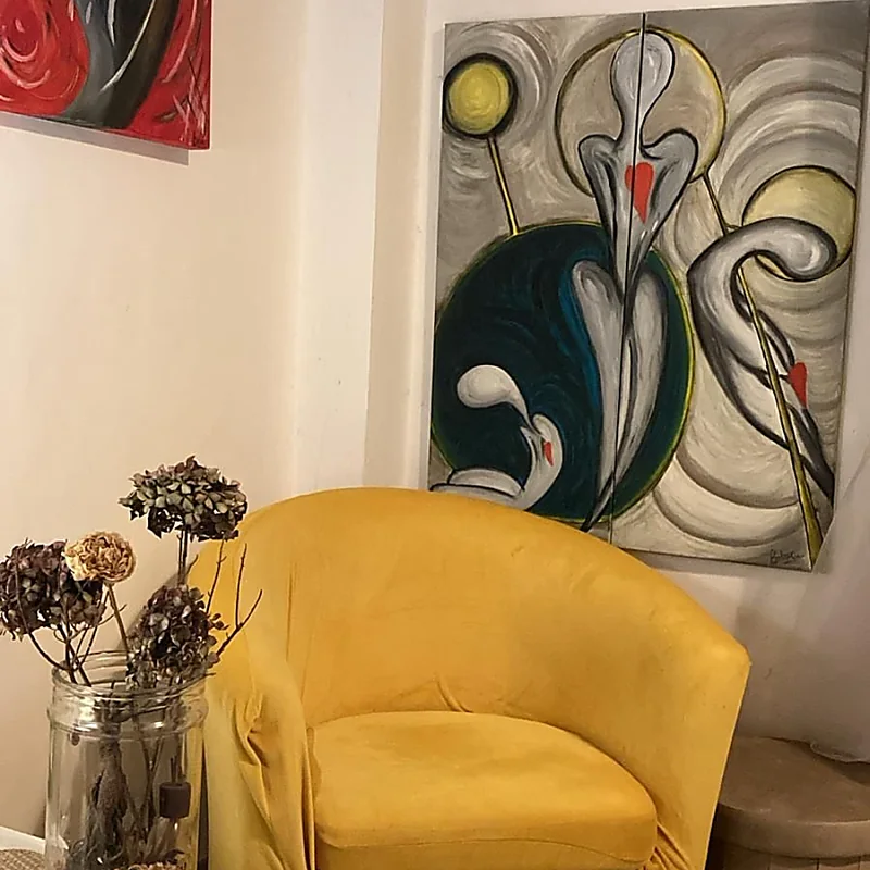 Angolo dello studio con poltrona gialla, fiori secchi e quadri